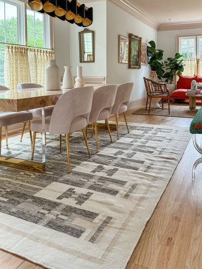 A home setting where a dining room is featured with a beautiful close up of a hand made large area rug in ivory , saige,  olive and taupe shades andin the far back a red sofa is looking like a professional interiordesigners home