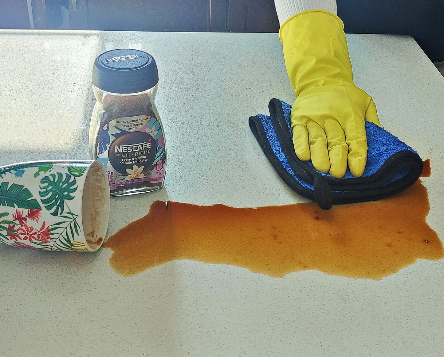 A wonderful display showing how the towel quickly absorberf the spilled coffee on the kitchen top a person wiping with no effort wearing a yello glove