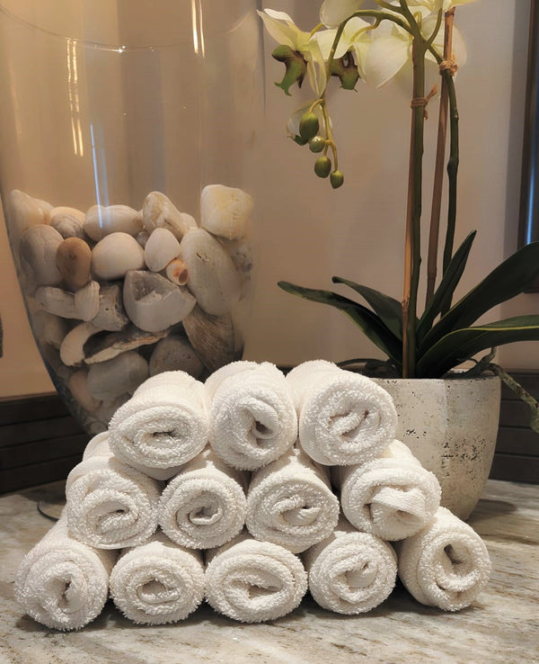 12 white coton face towels nicely folded and stacked on the top of each other making like a pyramid ina bathroom setting
