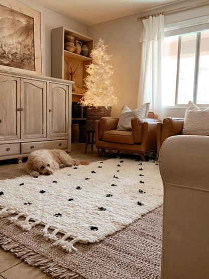 Layerd rugs in pure wool with crochet technique in a good texture with a dog resting on it ina cosy beige home living room setting with a whit chiristmas lit in the one corner and brown leather sofas.