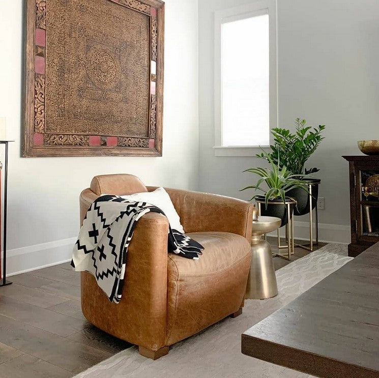 Modern living room with a brown leather armchair draped with a black and white geometric Faith Organic Cotton Throw Blanket. Eco-friendly, stylish, and soft, this throw comes with a free matching pillow for a limited time. Perfect for cozy home décor.