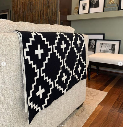 Faith Organic Cotton Throw Blanket – Stylish black and white geometric patterned throw draped over a beige sofa in a modern living room. Made from 100% organic cotton, soft, breathable, and perfect for boho, farmhouse, or minimalist home décor.