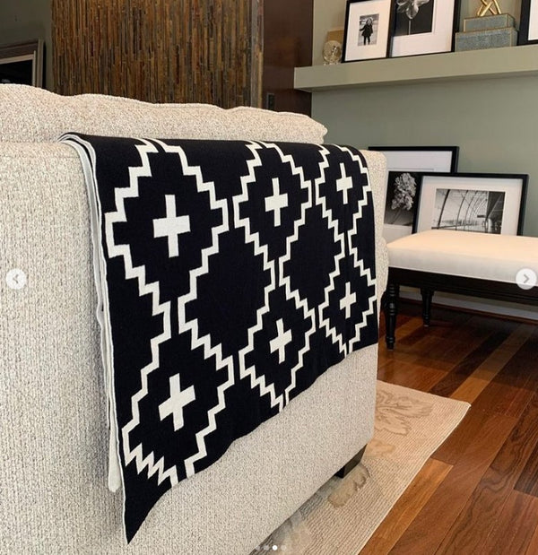 Faith Organic Cotton Throw Blanket – Stylish black and white geometric patterned throw draped over a beige sofa in a modern living room. Made from 100% organic cotton, soft, breathable, and perfect for boho, farmhouse, or minimalist home décor.