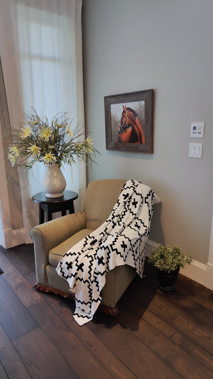 Faith Organic Cotton Throw Blanket with Free Matching Pillow – Soft black and white geometric patterned throw draped over a cozy armchair. Made from 100% organic cotton, perfect for modern, farmhouse, and boho-style home décor. Limited-time offer: Free matching pillow included!