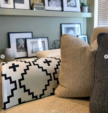 Faith Organic Cotton Throw Blanket in black and white geometric design draped over a neutral-toned sofa. Cozy, modern living room setup with framed black-and-white photography and earthy décor. Free matching pillow included for a limited time.