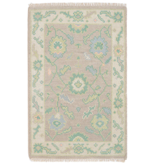 A rectangular wool 2x3 ft oushak mini woven rug with a traditional floral pattern in muted pastel tones of sage green, light blue, and soft yellow on a warm beige background, finished with a fringed edge.