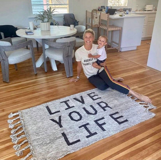 Amanda kloots and her sonis smiling and sitting on the floor on the unique bespoke hand made area rug in pure wool saying Live you life by Rich clas decor